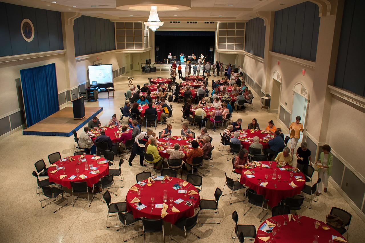 A large group of older individuals in a large room sitting at red circular tables